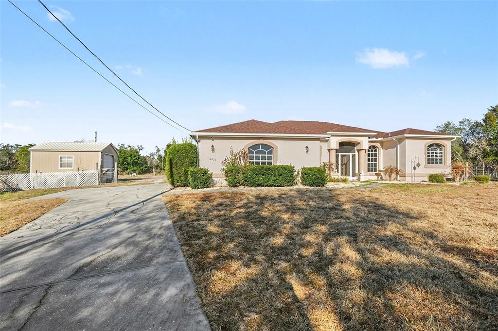 A single-story house with a tan stucco exterior and a detached metal shed — 16031 DONNEY MOOR LANE, SPRING HILL, FL