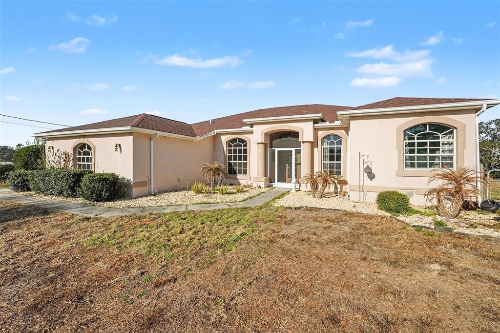 A single-story house with a beige stucco exterior, a brown roof, and arched windows — 16031 DONNEY MOOR LANE, SPRING HILL, FL
