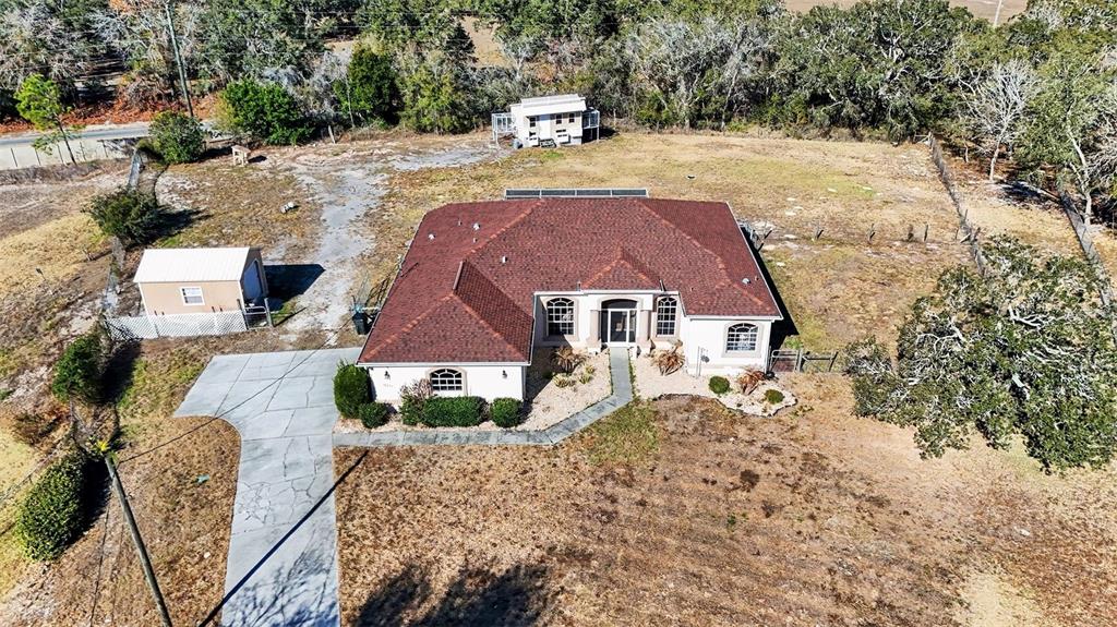 An aerial view shows a single-story house with a red roof, driveway, and two sheds — 16031 DONNEY MOOR LANE, SPRING HILL, FL