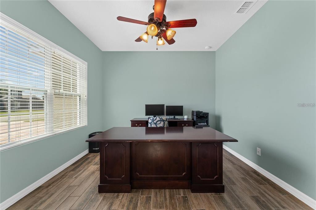 A home office features light blue walls, wood-look tile flooring, and a large dark wood desk — 14537 SAN LORENZO DRIVE, ORLANDO, FL