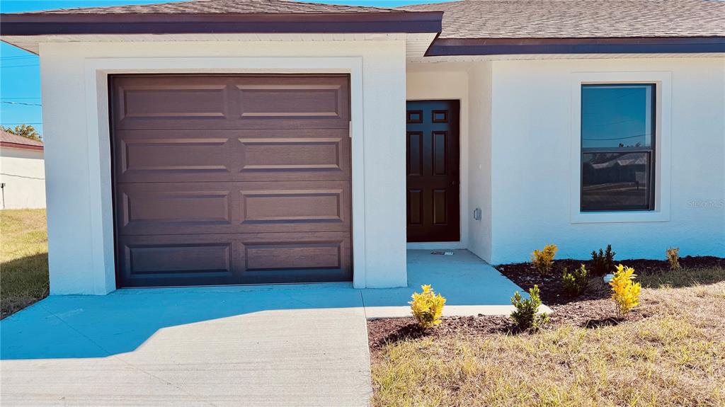 A white house exterior features a brown garage door, a dark front door, and landscaping — 27063 WASHINGTON STREET, PUNTA GORDA, FL