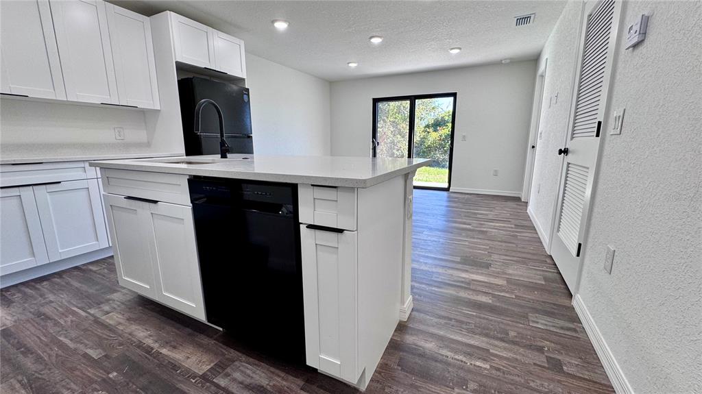 A modern kitchen features white cabinets, a central island with a dishwasher, and wood-look flooring — 27063 WASHINGTON STREET, PUNTA GORDA, FL
