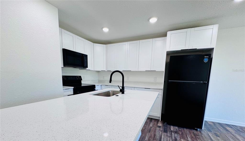 A modern kitchen features white cabinets, quartz countertops, a kitchen island, and black appliances — 27063 WASHINGTON STREET, PUNTA GORDA, FL