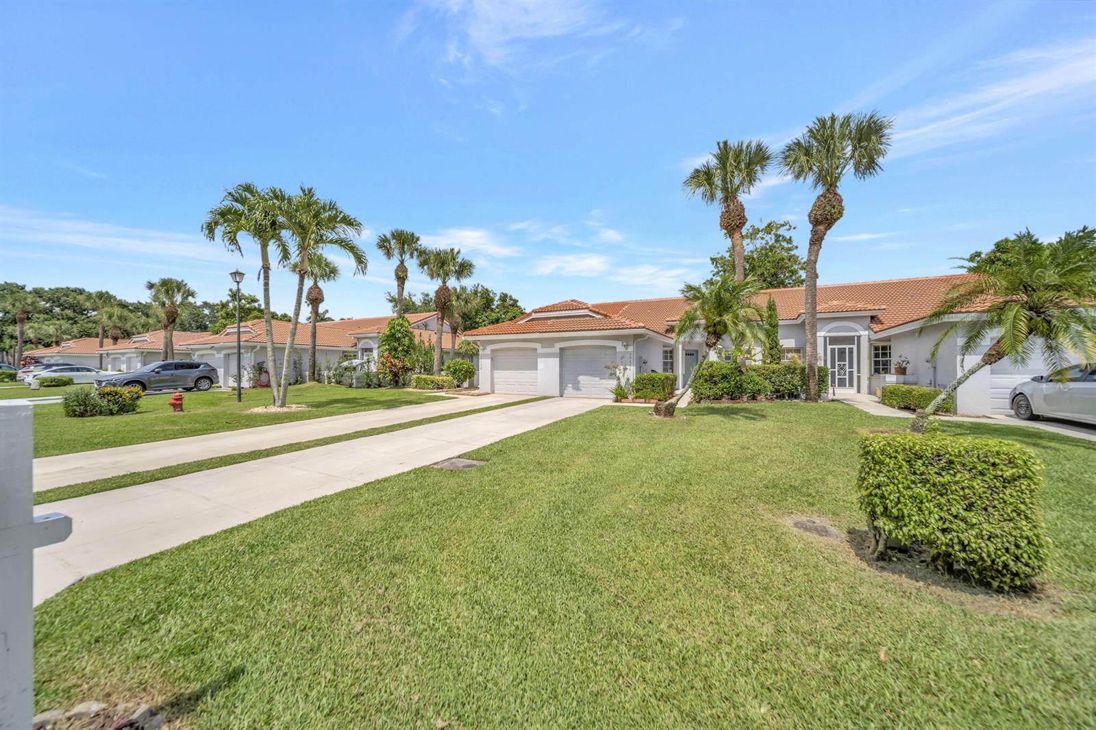 A single-story house with a two-car garage, palm trees, and a green lawn — 15136 W Tranquility Lake Drive, Delray Beach FL 33446, DELRAY BEACH, FL