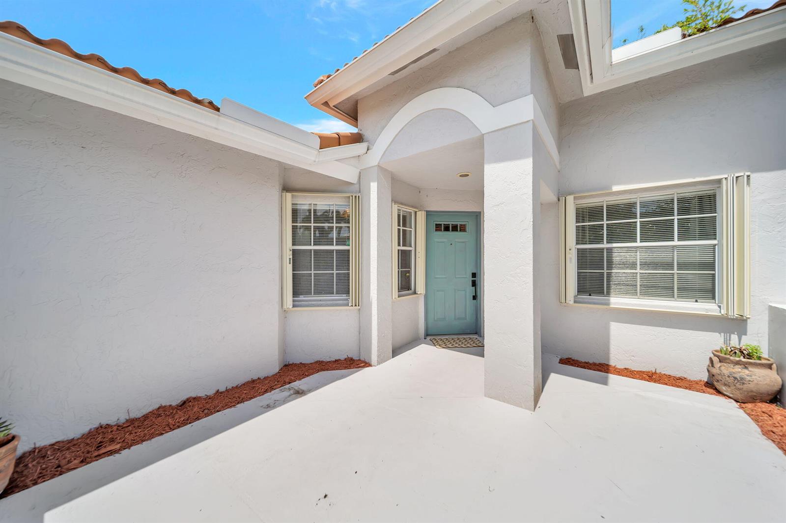 A light blue front door is centered under a covered entryway with white stucco walls — 15136 W Tranquility Lake Drive, Delray Beach FL 33446, DELRAY BEACH, FL