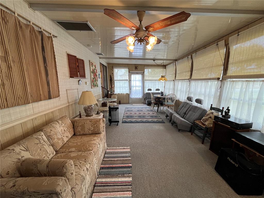A sunroom features a ceiling fan, carpeted flooring, a floral sofa, and large windows — 16 GREY FOX LANE, LAKE WALES, FL