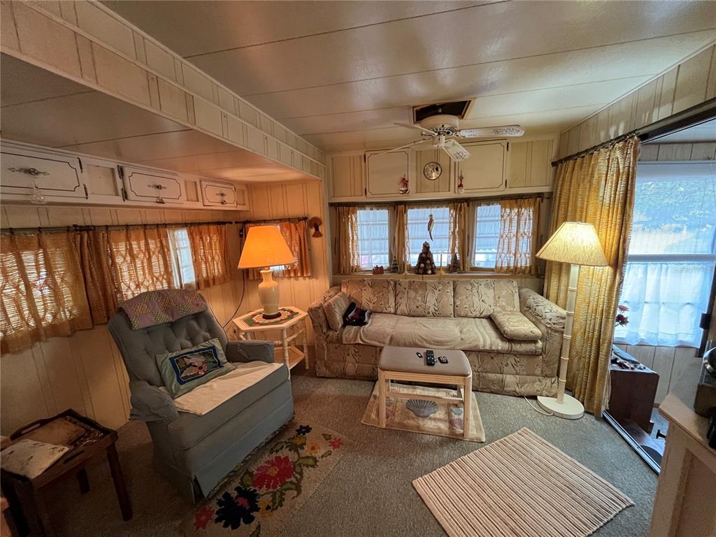 A living room with wood-paneled walls, a sofa, a recliner, and yellow curtains — 16 GREY FOX LANE, LAKE WALES, FL