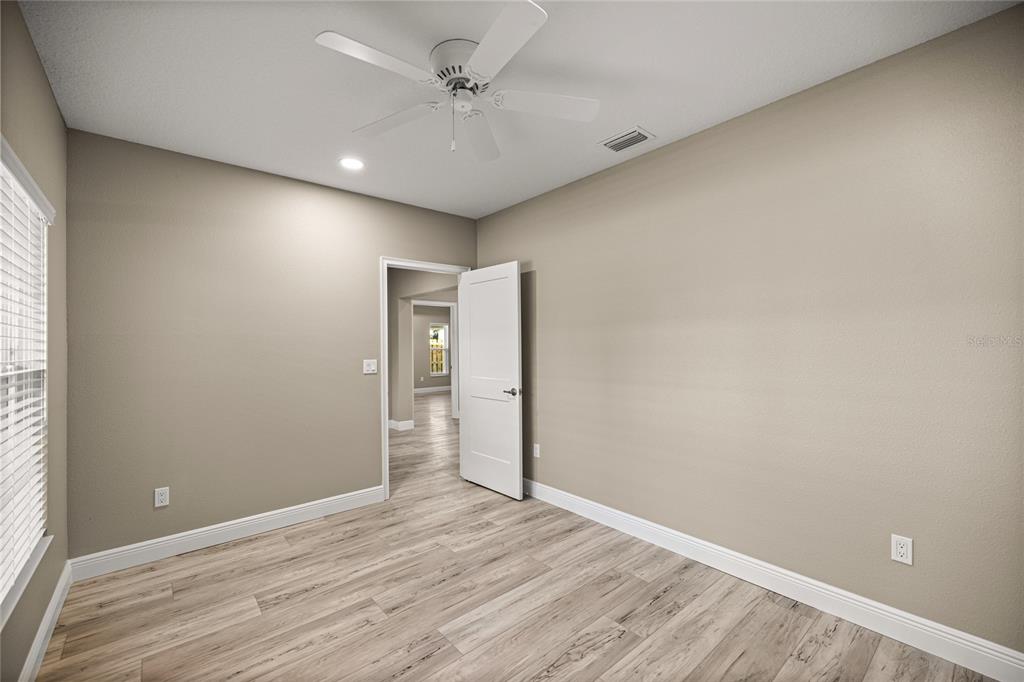 An empty bedroom features light-colored wood-look flooring, beige walls, a ceiling fan, and an open door — 2315 SE 31ST PLACE, OCALA, FL