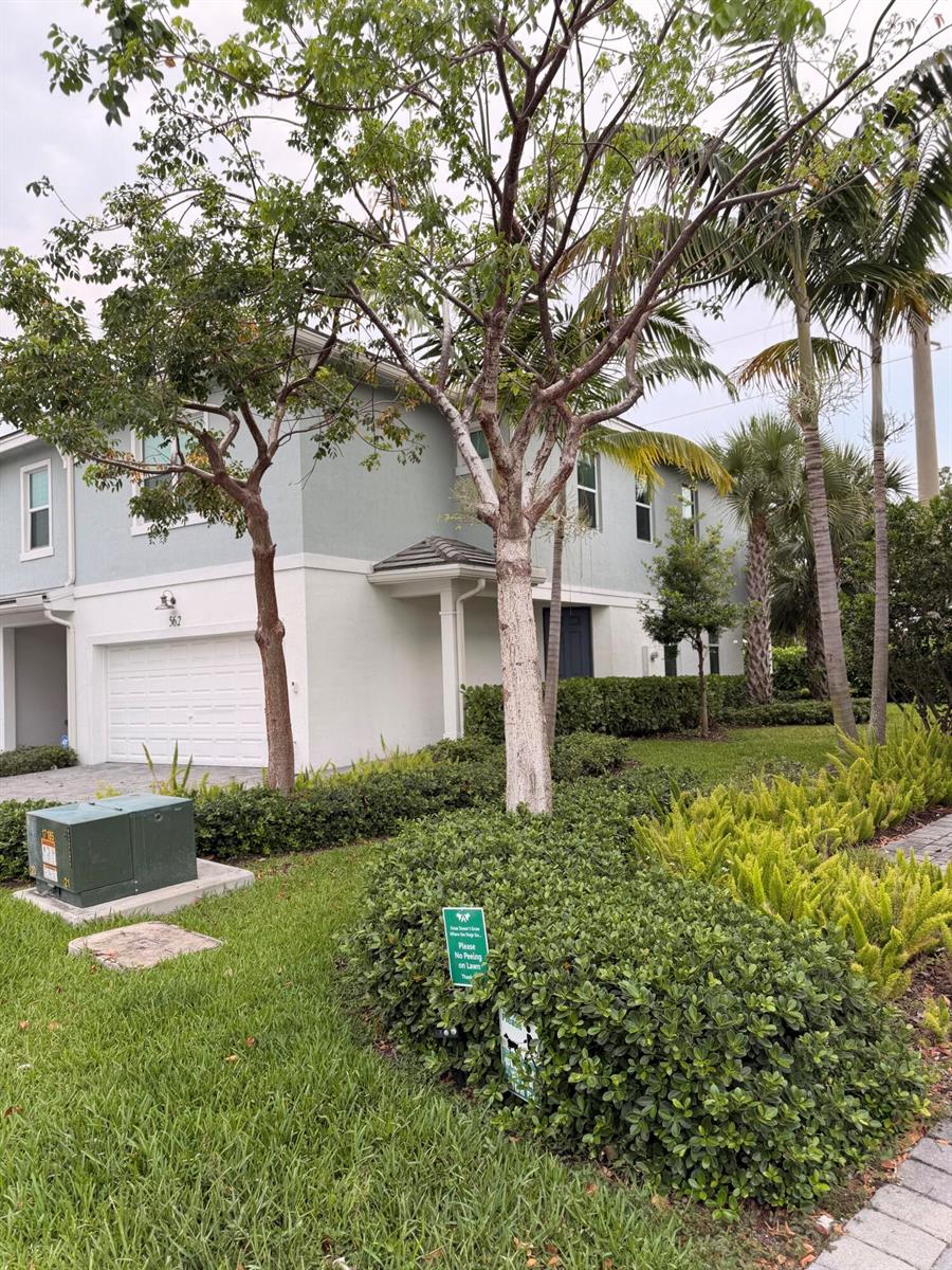 A two-story house with a white garage and a green lawn featuring a small sign — 562 Parsons Way, Deerfield Beach FL 33442, DEERFIELD BEACH, FL