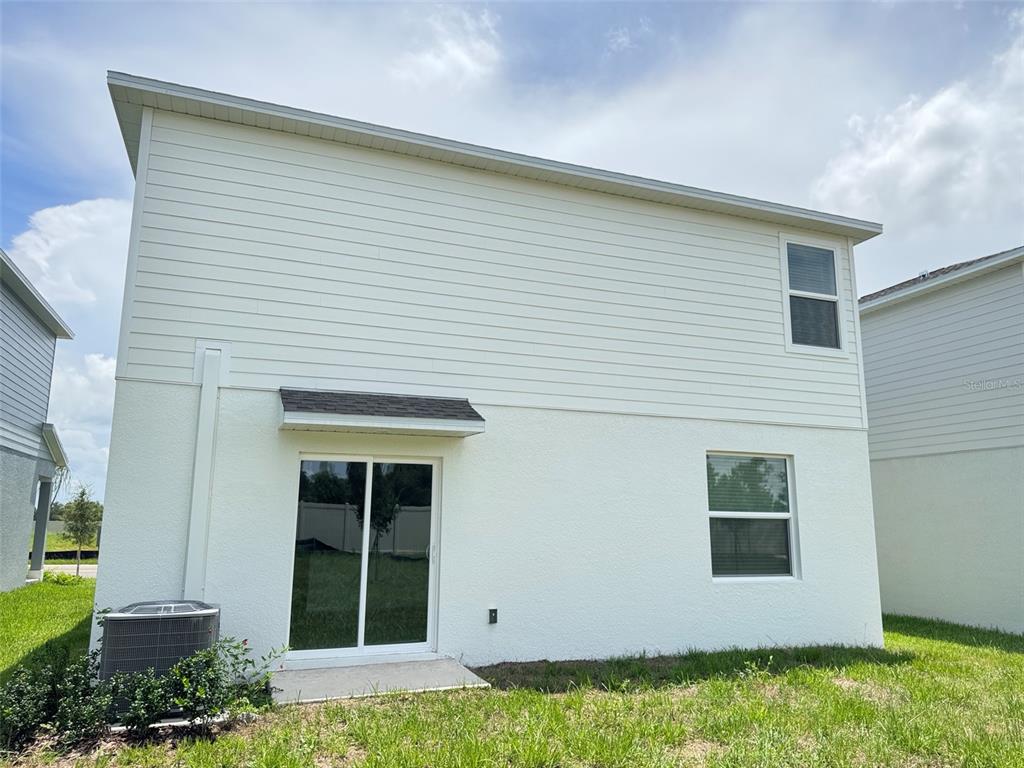 The rear exterior of a two-story house features white siding, stucco walls, and a sliding door — 11877 NOBLE CHASE PATH, DADE CITY, FL