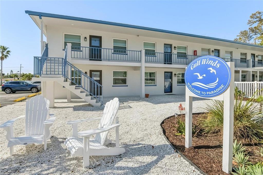 A two-story motel building with white siding, blue railings, and white Adirondack chairs in front — 2308 1ST STREET UNIT 1, INDIAN ROCKS BEACH, FL