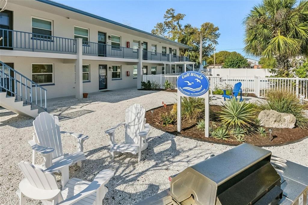 An exterior view of a two-story apartment building with a gravel courtyard and patio chairs — 2308 1ST STREET UNIT 1, INDIAN ROCKS BEACH, FL