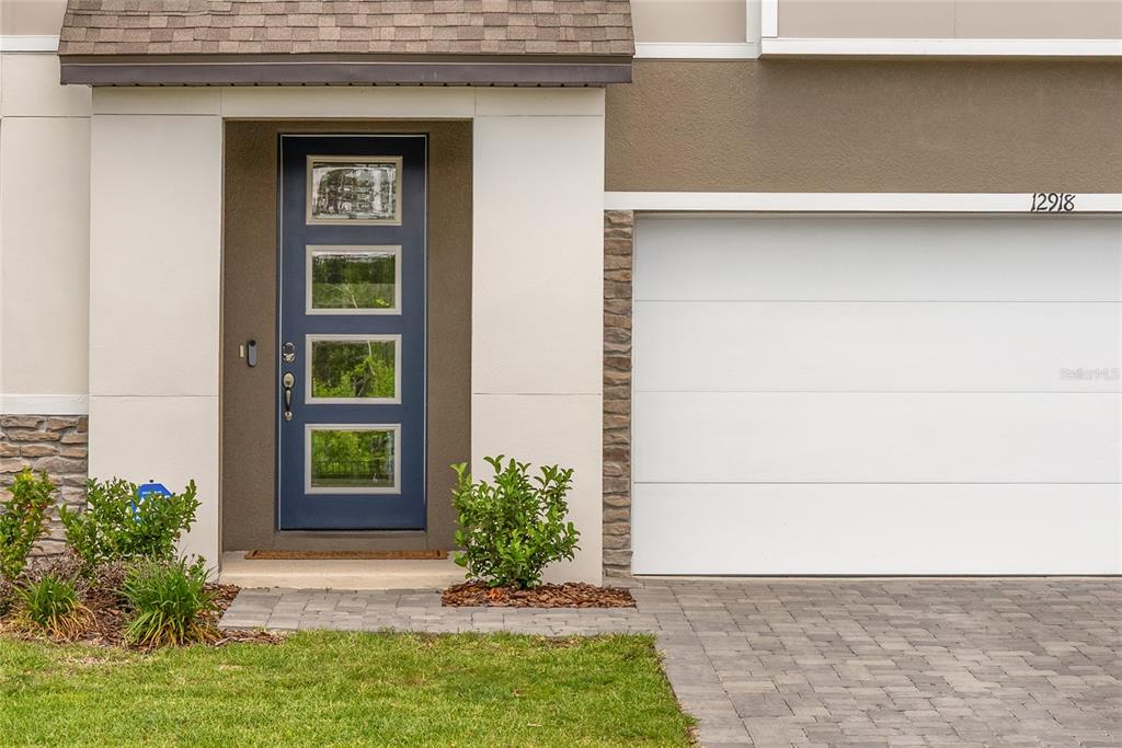 A blue front door with four glass panels sits beside a white two-car garage — 12918 PROMISE PLACE, ORLANDO, FL