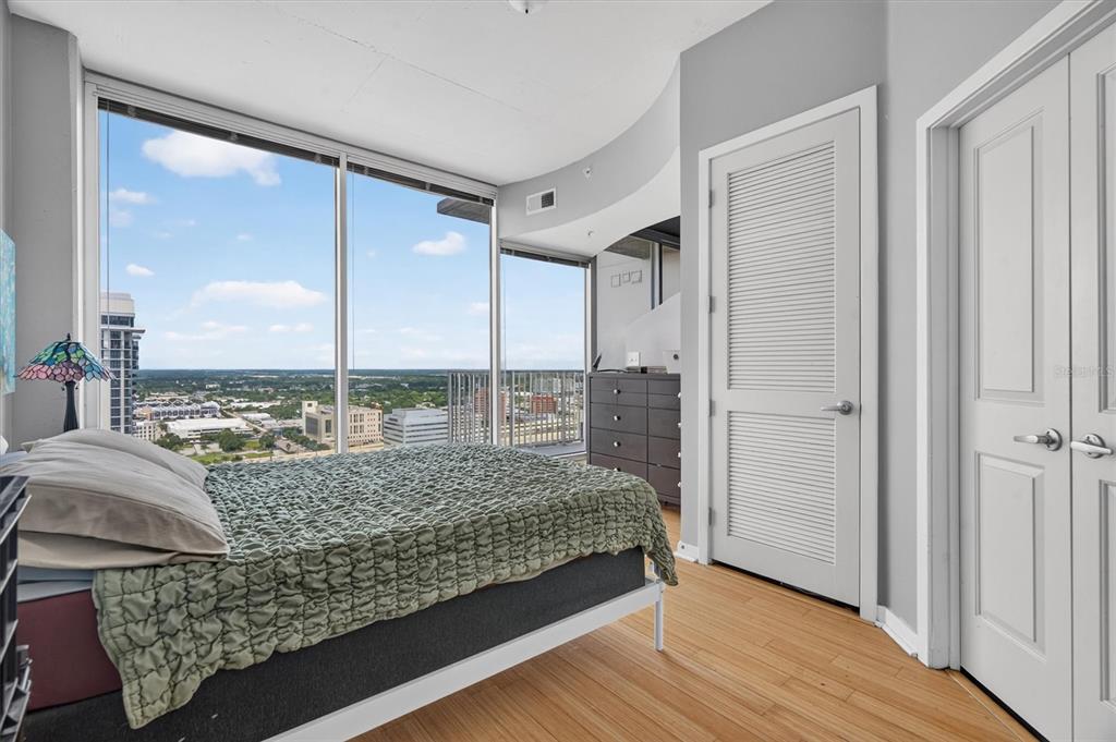 A bedroom with a bed, wood flooring, and floor-to-ceiling windows overlooking a city skyline — 155 S COURT AVENUE UNIT 2514, ORLANDO, FL