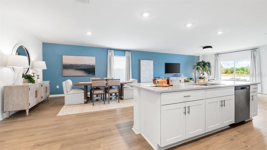 An open-concept kitchen and dining area features white cabinetry, light wood flooring, and blue walls — 5430 ISLA SAONA DRIVE, KISSIMMEE, FL