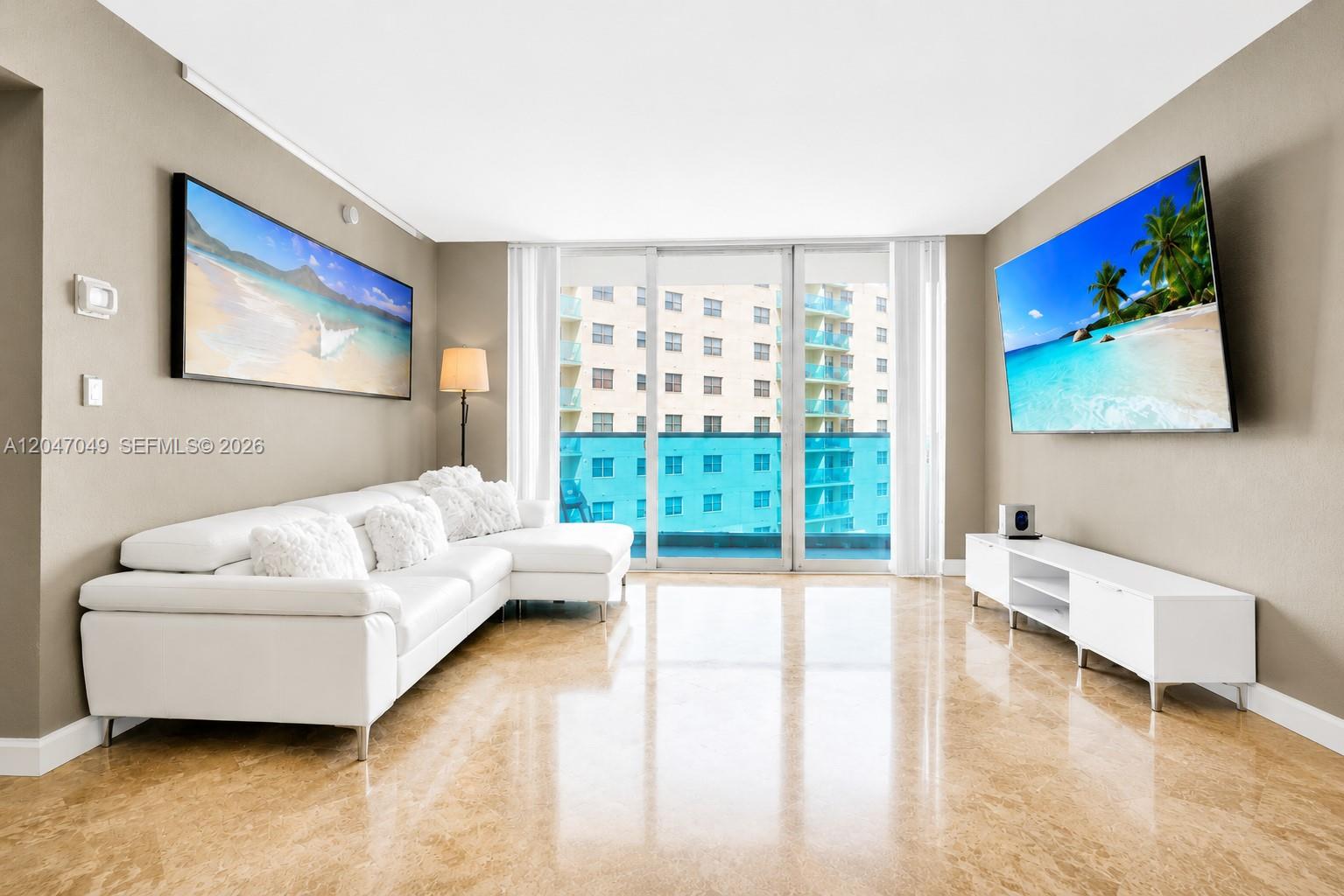 A living room features a white sectional sofa, a wall-mounted television, and marble flooring — 4001 S Ocean Dr # 11M, Hollywood FL 33019, HOLLYWOOD, FL