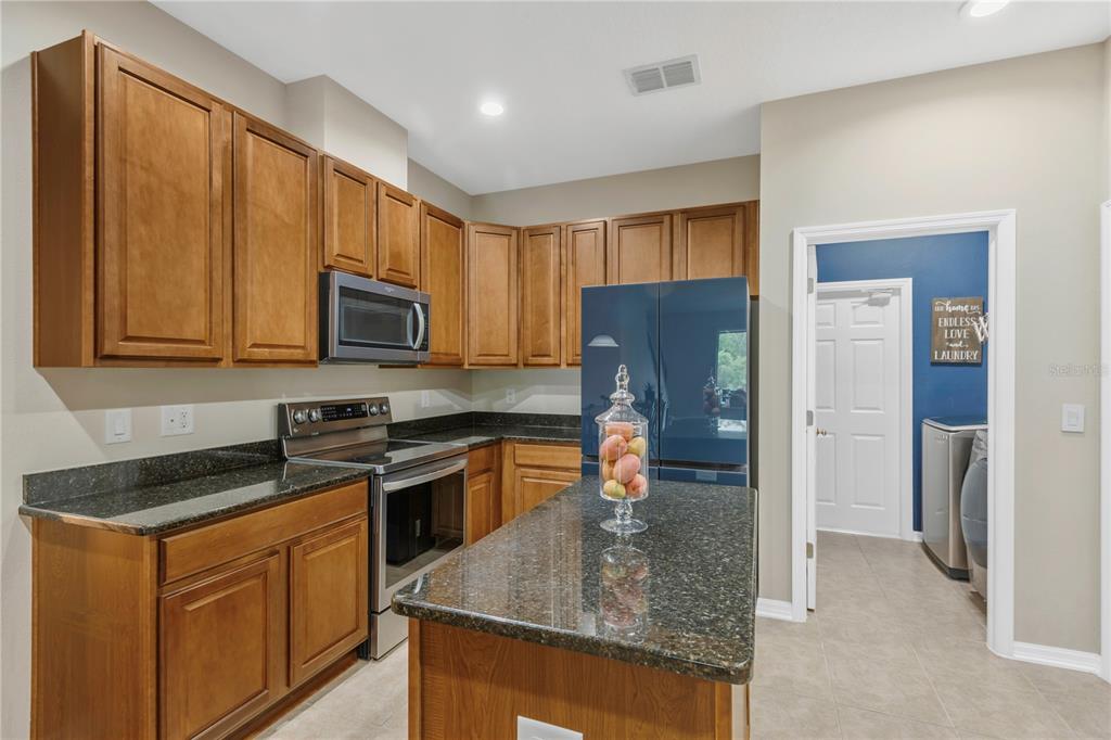 A kitchen with wood cabinets, dark granite countertops, stainless steel appliances, and a center island — 10859 BREAKING ROCKS DRIVE, TAMPA, FL