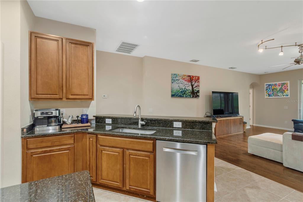 A kitchen with wood cabinets, dark granite countertops, and stainless steel appliances overlooks a living area — 10859 BREAKING ROCKS DRIVE, TAMPA, FL