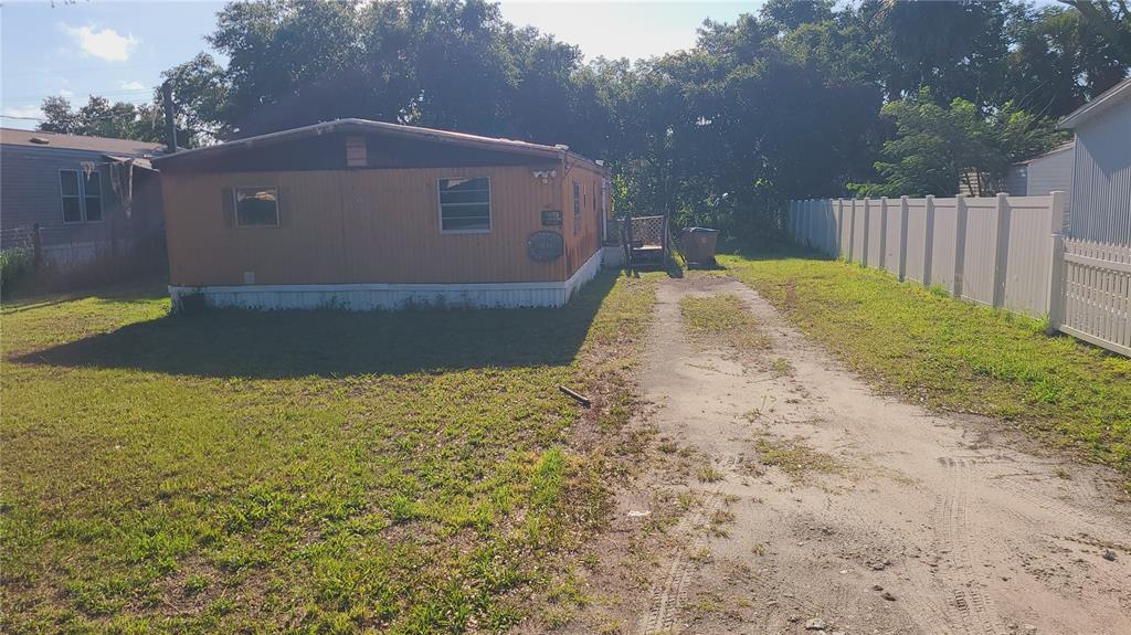 An exterior view of a single-story mobile home with a dirt driveway and white fence — 1683 MAGNOLIA LANE, KISSIMMEE, FL
