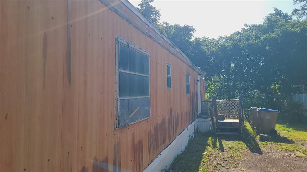 The exterior side of a mobile home features orange metal siding and a small wooden staircase — 1683 MAGNOLIA LANE, KISSIMMEE, FL