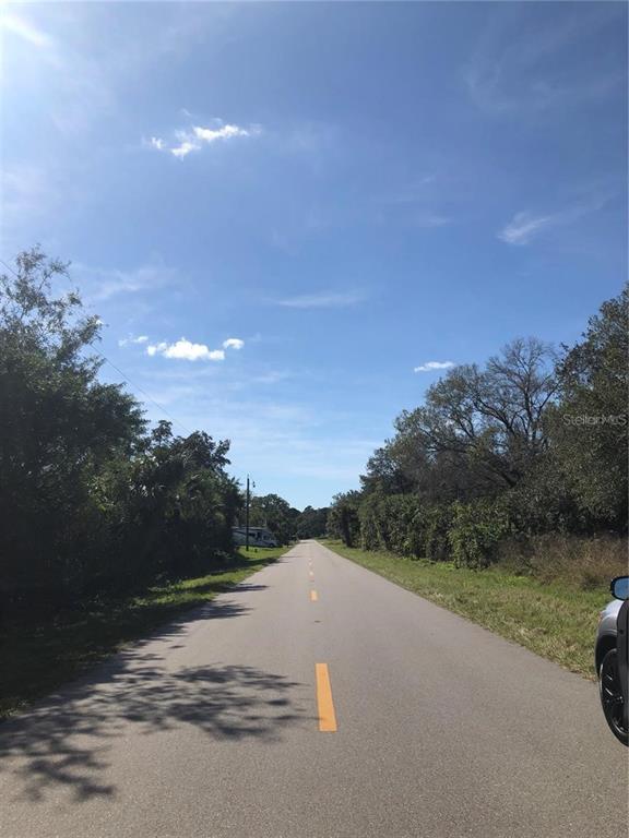 A paved road with a yellow center line stretches through a wooded area under blue skies — 1197 EPPINGER DRIVE, PORT CHARLOTTE, FL