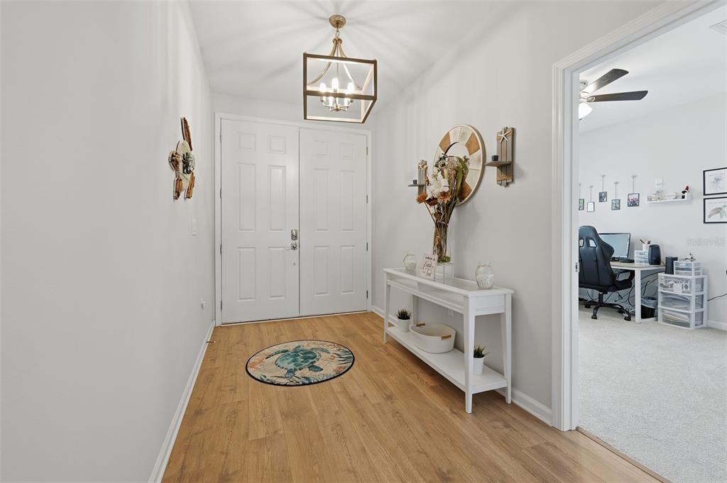 A bright entryway features light wood flooring, a white console table, and a modern chandelier — 500 GRAND LANDINGS PARKWAY, PALM COAST, FL