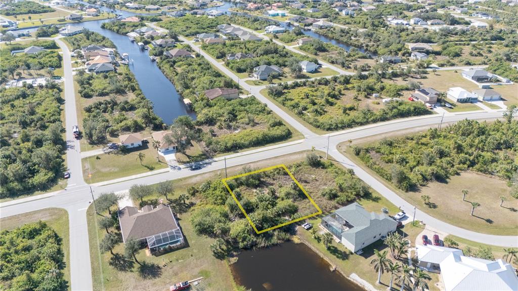An aerial view shows a vacant, rectangular residential lot outlined in yellow near a canal — 14386 INGRAHAM BOULEVARD, PORT CHARLOTTE, FL