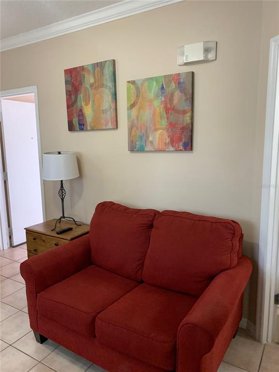 A red loveseat sits in front of a wall with two abstract paintings and a lamp — 2777 N POINCIANA BOULEVARD UNIT 301B, KISSIMMEE, FL