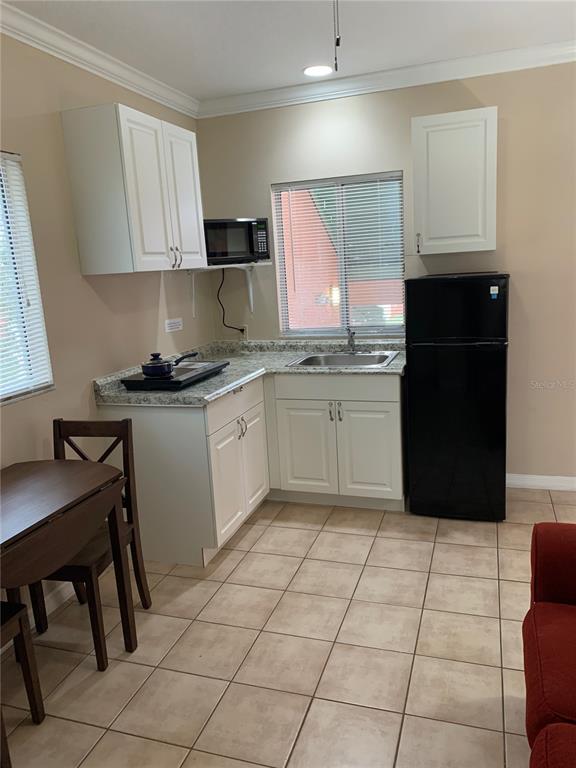 A small kitchen features white cabinets, granite countertops, a black refrigerator, and tile flooring — 2777 N POINCIANA BOULEVARD UNIT 301B, KISSIMMEE, FL