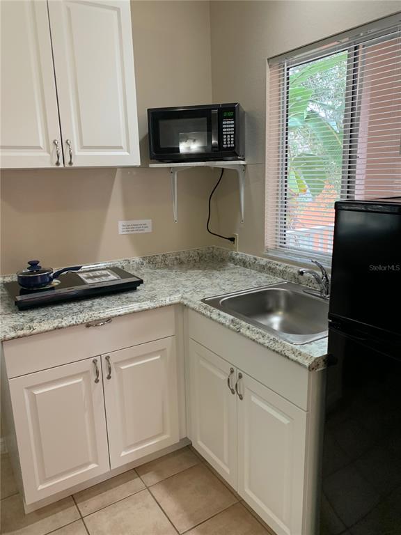 A small kitchen features white cabinets, granite-look countertops, a sink, a microwave, and a cooktop — 2777 N POINCIANA BOULEVARD UNIT 301B, KISSIMMEE, FL
