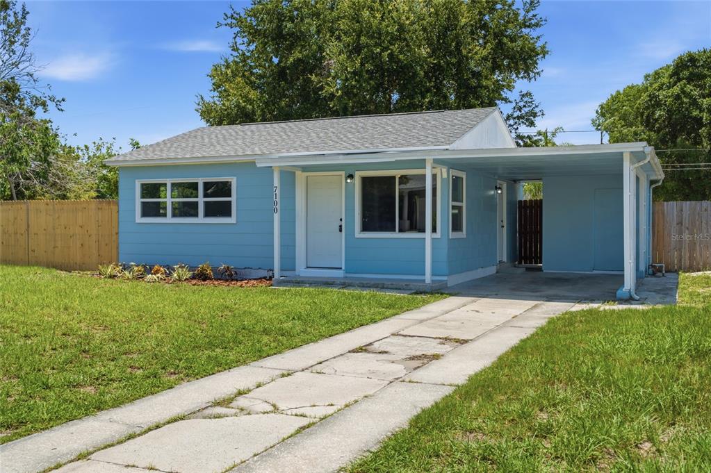 A light blue single-story house features a front porch, a carport, and a concrete driveway — 7100 13TH STREET N, ST PETERSBURG, FL