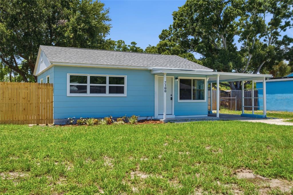 A light blue single-story house features a front porch, a carport, and a wooden fence — 7100 13TH STREET N, ST PETERSBURG, FL