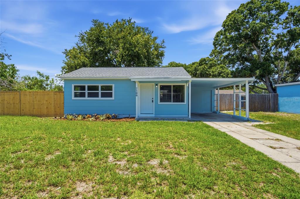 A light blue single-story house with a white door, a carport, and a grassy yard — 7100 13TH STREET N, ST PETERSBURG, FL