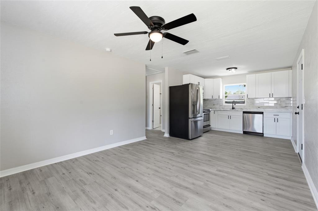 An open-concept kitchen and dining area features white cabinets, stainless appliances, and gray flooring — 7100 13TH STREET N, ST PETERSBURG, FL