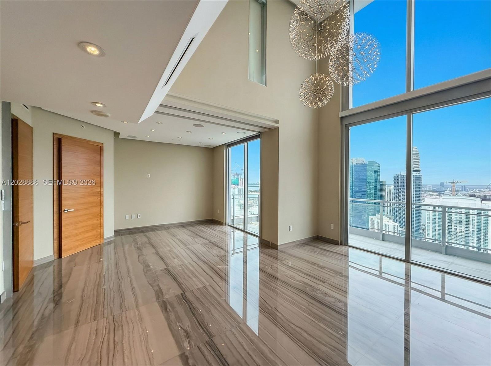 A modern, high-ceilinged living room features polished marble floors, floor-to-ceiling windows, and spherical chandeliers — 92 SW 3rd St, Miami FL 33130, MIAMI, FL