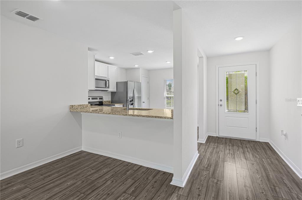 An open-concept kitchen with granite countertops overlooks a dining area near a white front door — 48 HERRING COURT, POINCIANA, FL