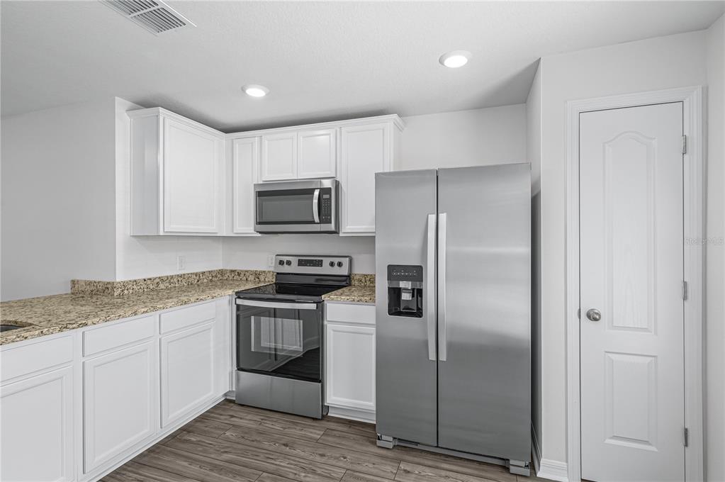 A kitchen features white cabinets, granite countertops, stainless steel appliances, and wood-look flooring — 48 HERRING COURT, POINCIANA, FL