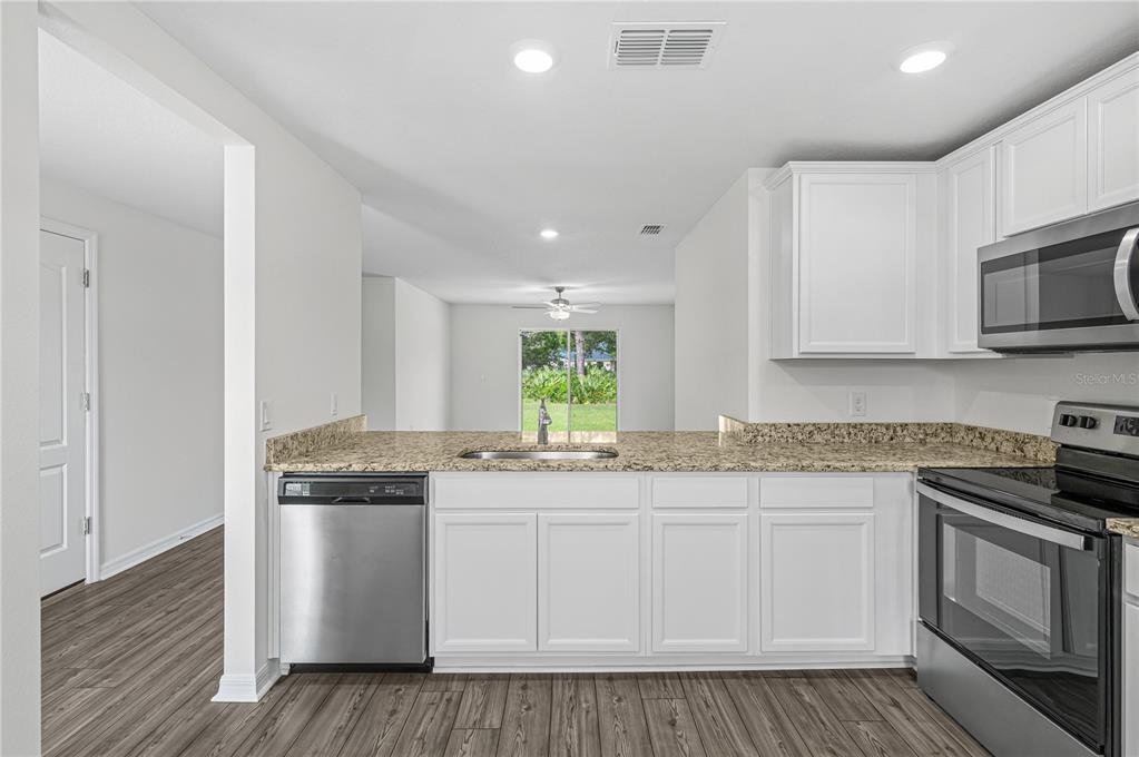 A kitchen with white cabinets, granite countertops, stainless steel appliances, and wood-look flooring — 48 HERRING COURT, POINCIANA, FL