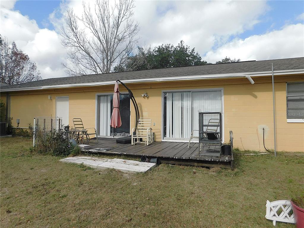A yellow house exterior features a wooden deck with sliding glass doors and patio furniture — 3610 SW 150TH LANE ROAD, OCALA, FL