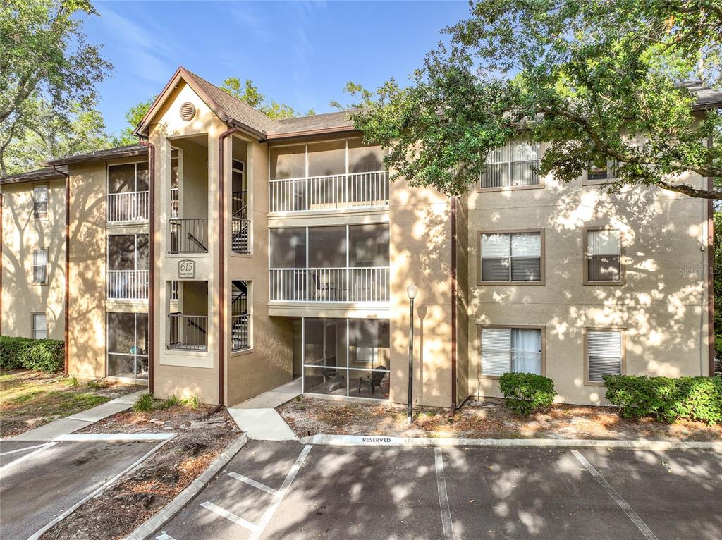 A three-story apartment building with tan stucco walls, screened balconies, and a parking lot — 615 DORY LANE UNIT 303, ALTAMONTE SPRINGS, FL