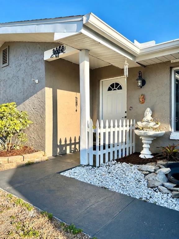 The exterior of a house features a white front door, a white picket fence, and a fountain — 1707 IRONWOOD COURT E, OLDSMAR, FL