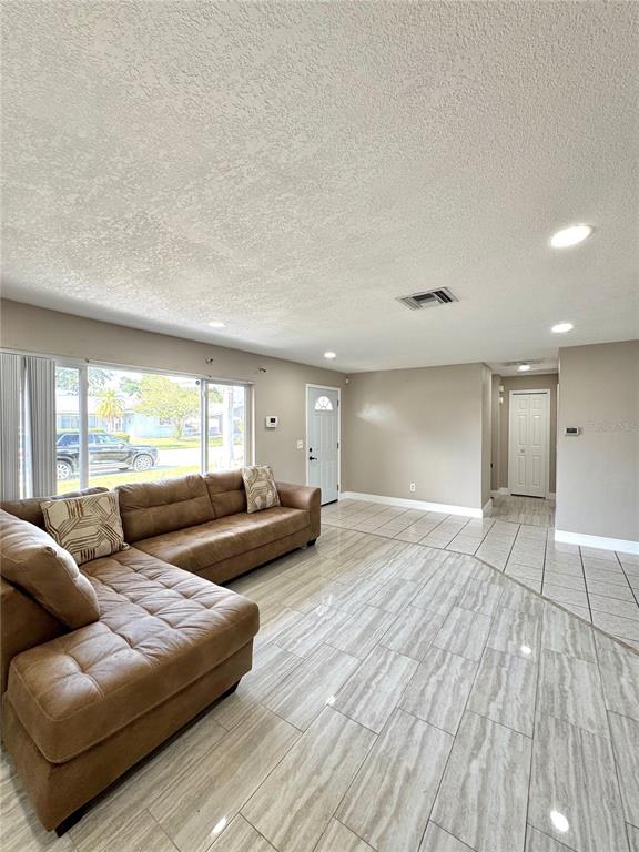 A living room with a brown sectional sofa, light tile flooring, and a white front door — 1707 IRONWOOD COURT E, OLDSMAR, FL