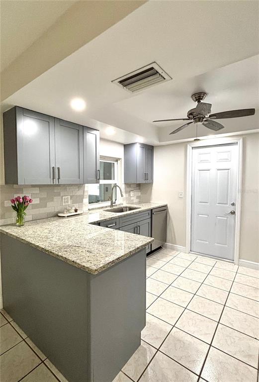 A kitchen features gray cabinets, granite countertops, a tile backsplash, and a ceiling fan — 1707 IRONWOOD COURT E, OLDSMAR, FL