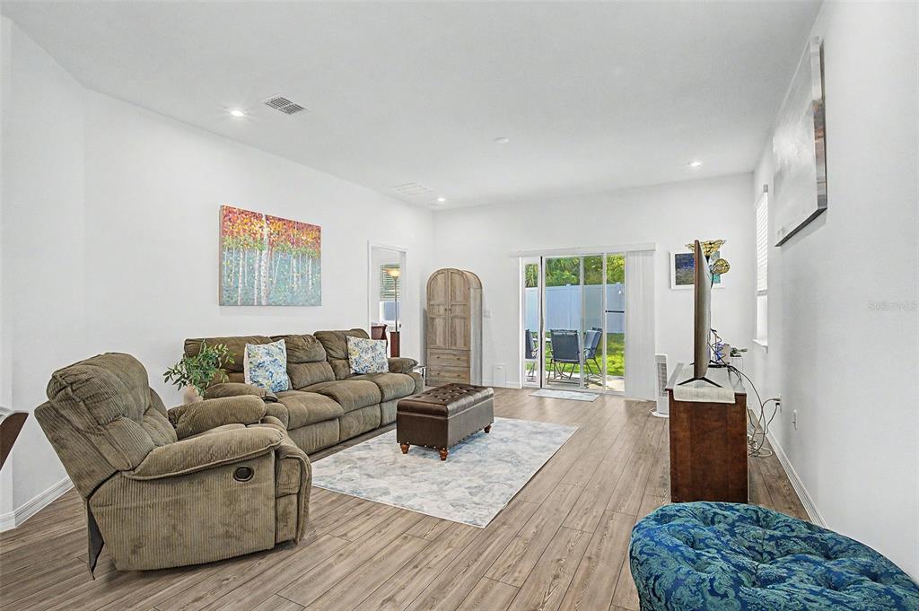A living room features wood-look flooring, a brown sofa, a recliner, and sliding glass doors — 703 ROCKAWAY LANE, COCOA, FL