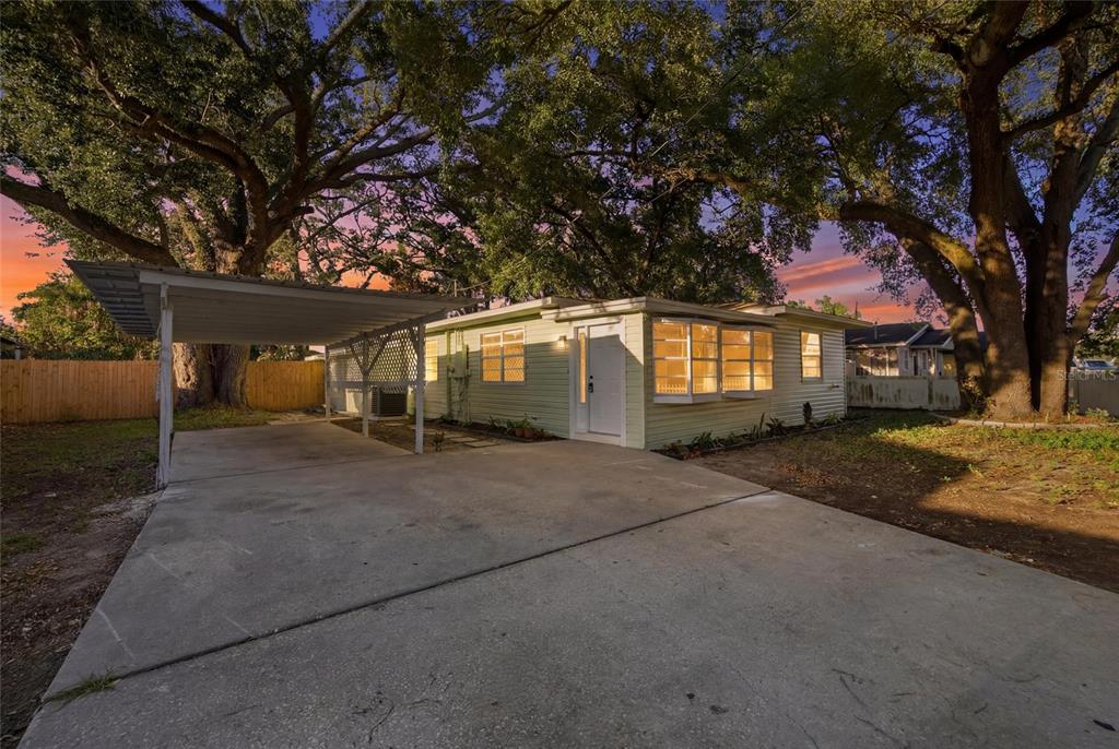 A light green single-story house with a carport and concrete driveway under large oak trees — 714 E 137TH AVENUE, TAMPA, FL