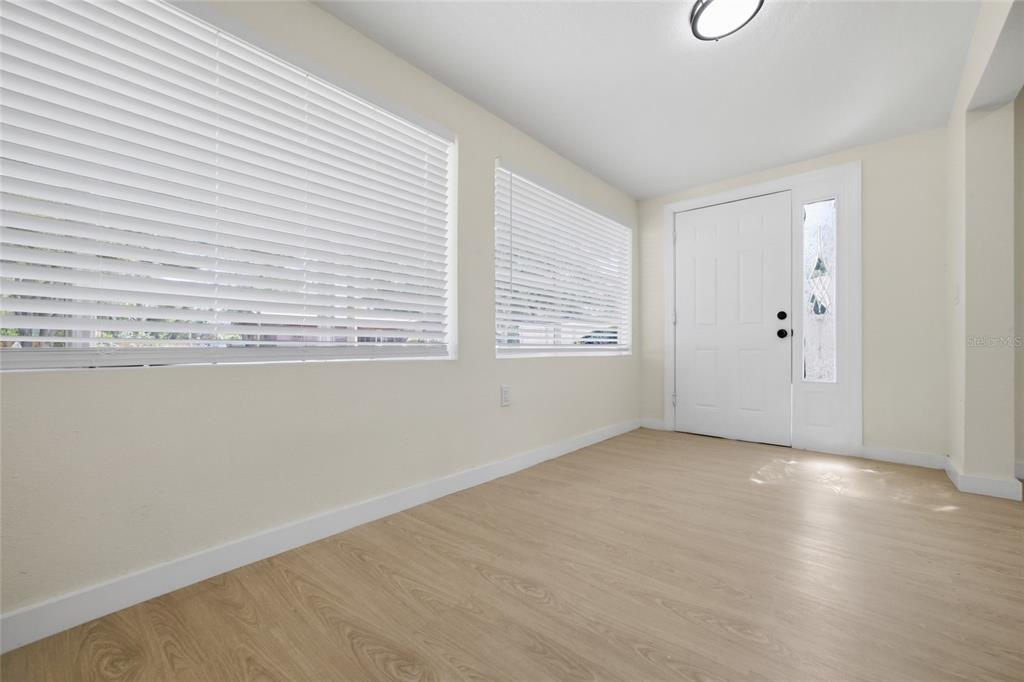 An empty room features light wood-look flooring, white walls, and two windows with blinds — 714 E 137TH AVENUE, TAMPA, FL