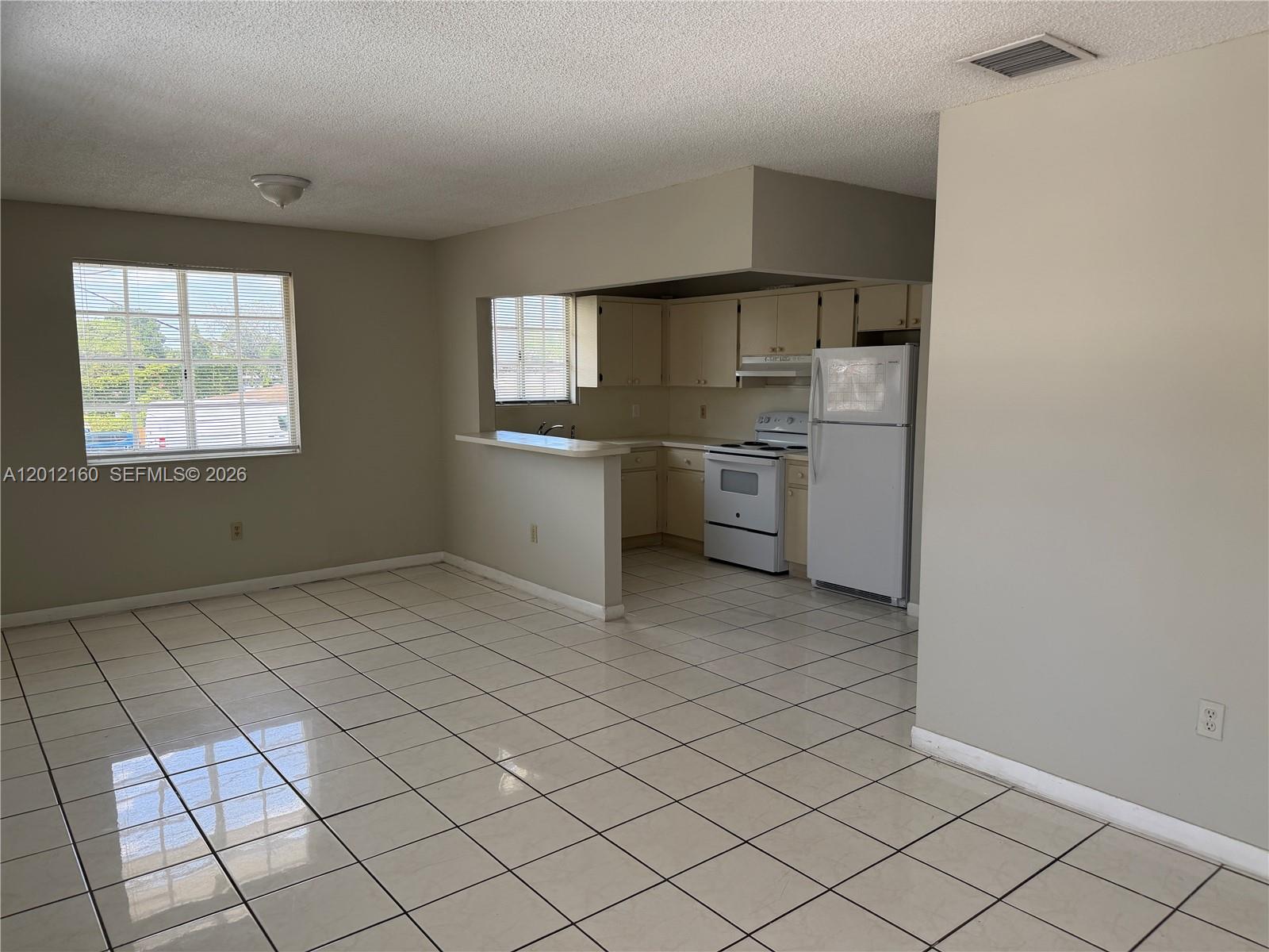 An open-concept kitchen with white appliances and tile flooring connects to a living area — 837 SE 8th Ct # 2, Hialeah FL 33010, HIALEAH, FL