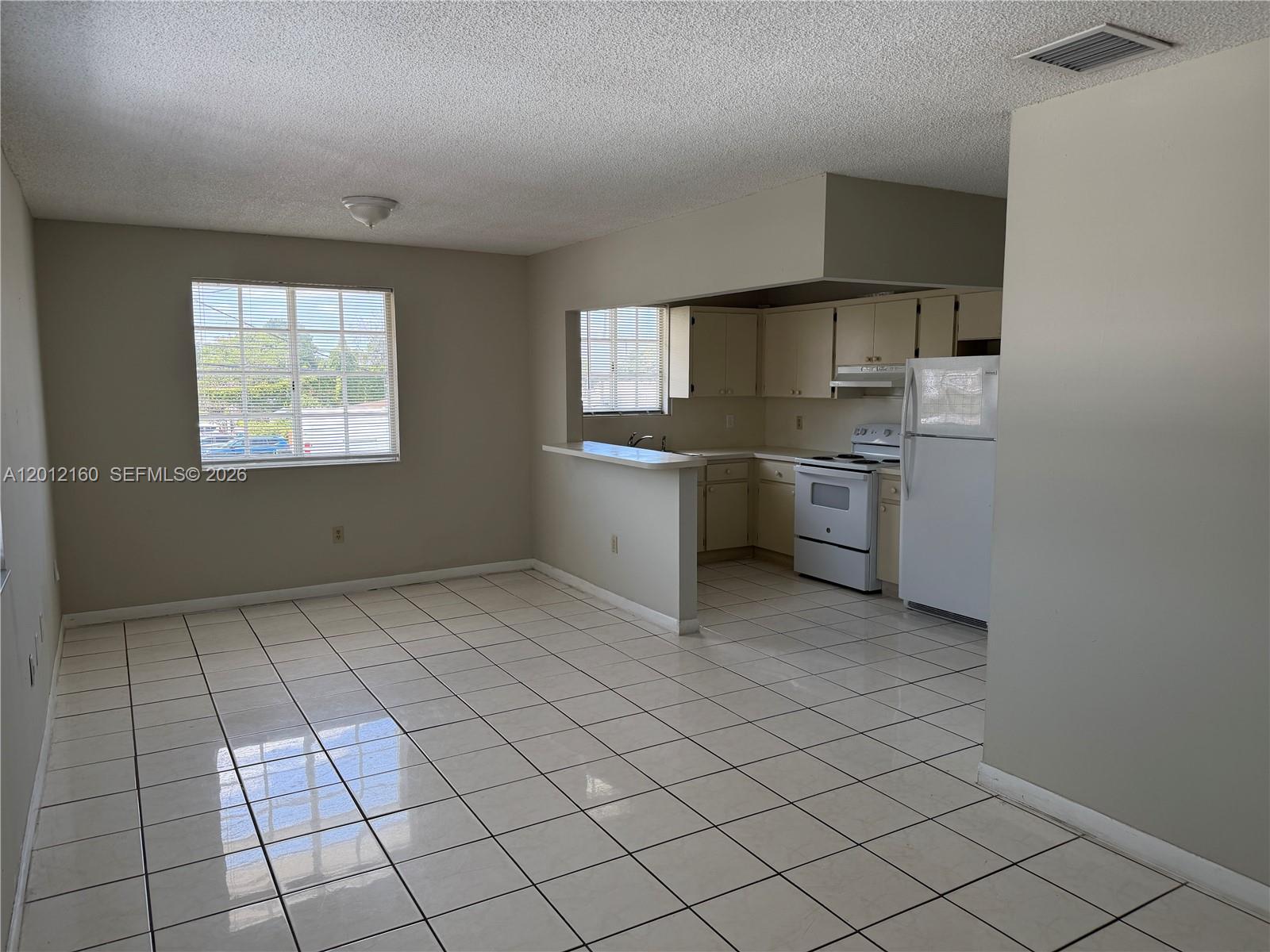 An open-concept kitchen and dining area features white tile flooring and light-colored cabinetry — 837 SE 8th Ct # 2, Hialeah FL 33010, HIALEAH, FL