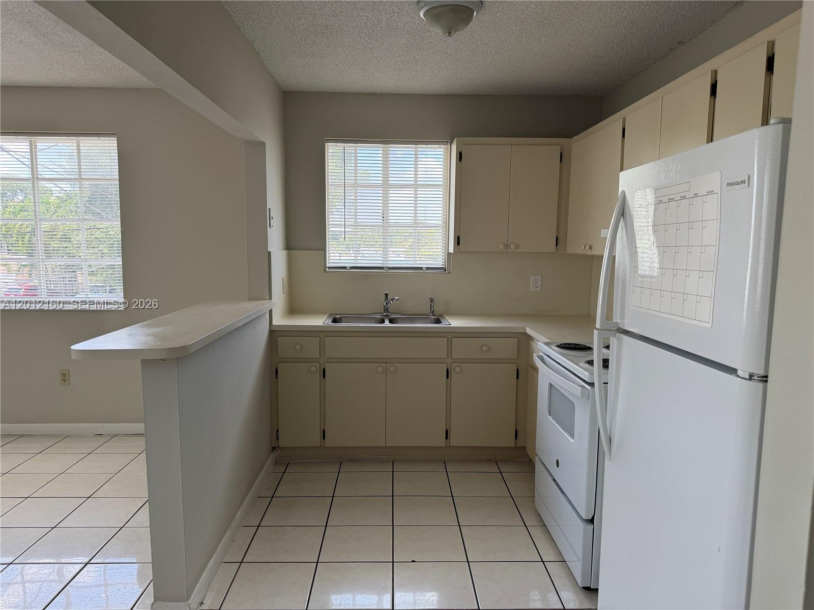 A kitchen features white appliances, beige cabinets, a double sink, and light-colored tile flooring — 837 SE 8th Ct # 2, Hialeah FL 33010, HIALEAH, FL