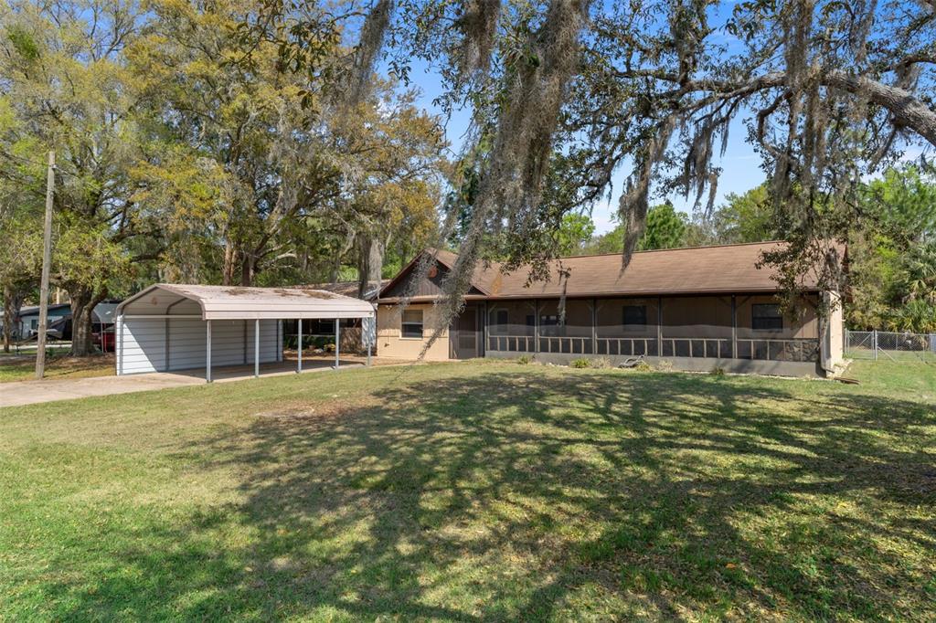 A single-story house with a screened-in porch and a detached metal carport on a lawn — 7095 W GREENWOOD LANE, CRYSTAL RIVER, FL